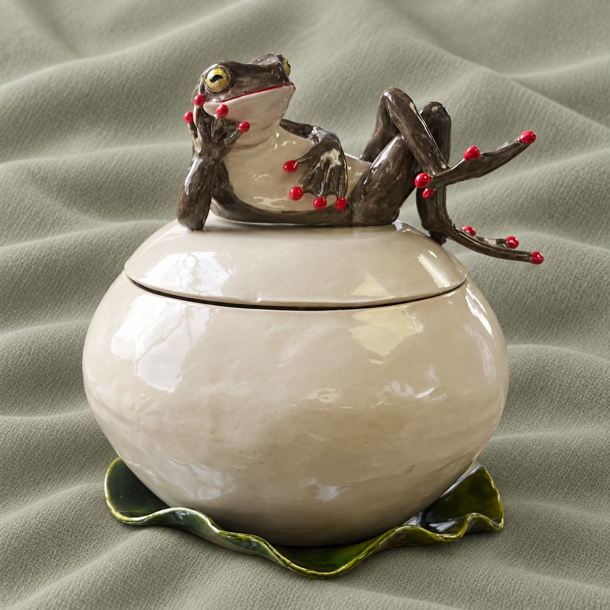 Ivory-coloured lidded ceramic jar with a reclining frog and green leaf base